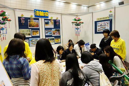 法轮功展位被来场者挤满，人们学折纸莲花并聆听介绍法轮功